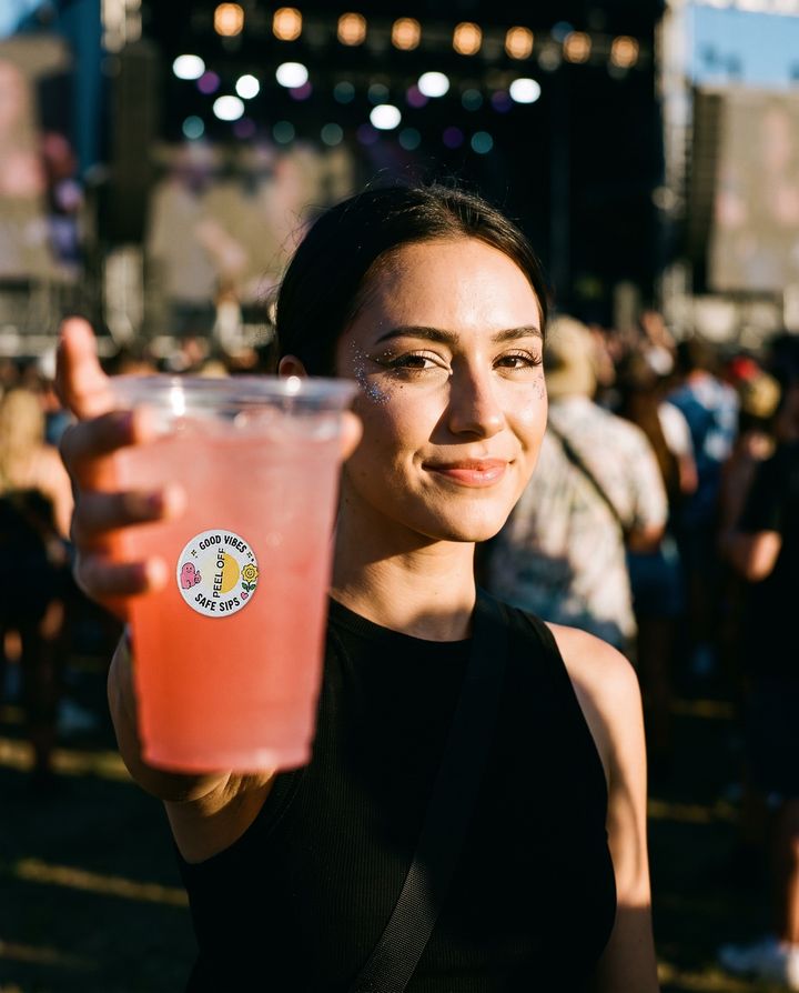 Festival-goer holding up a drink with a BeSuro™ sticker on the cup